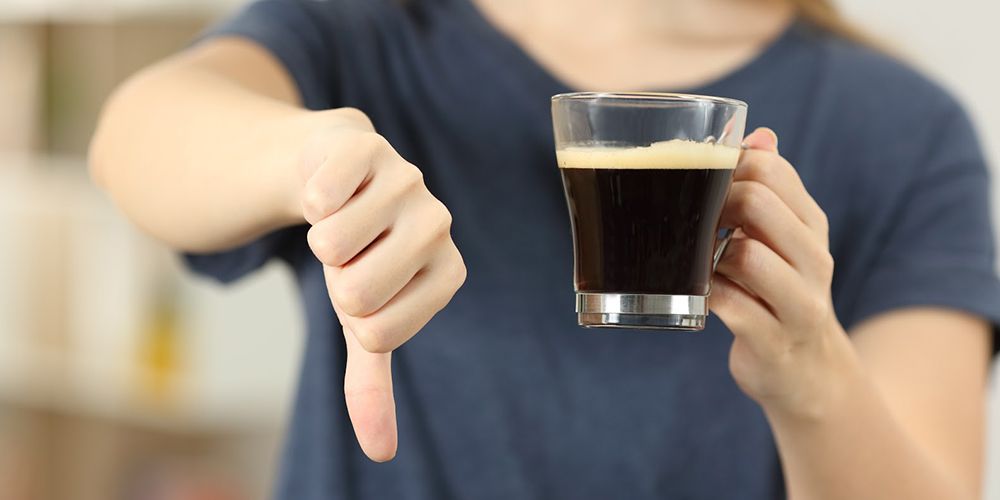 woman giving thumbs down signal while holding coffee
